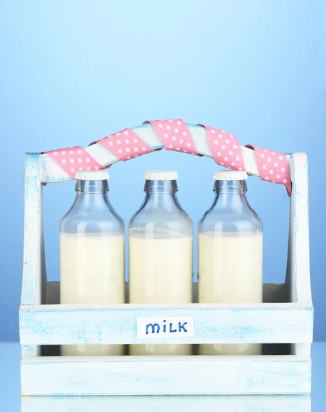 Milk in bottles in wooden box on blue background — Stock Photo, Image