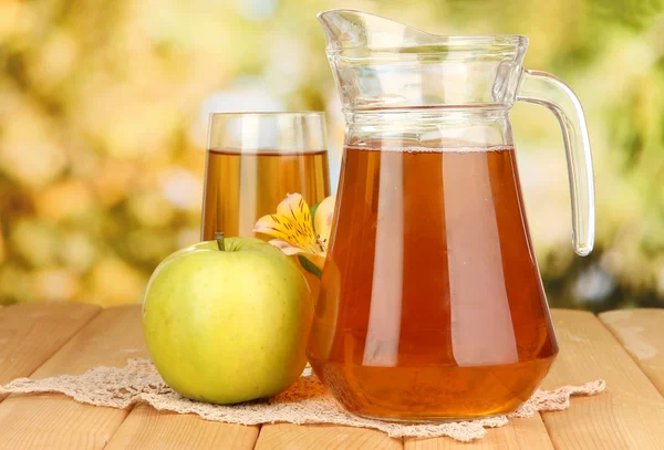 Fullt glas och kanna av äppeljuice och äpple på träbord utomhus — Stockfoto