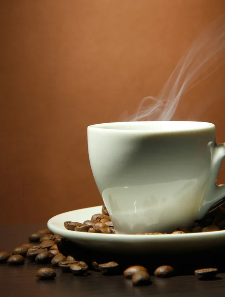 Tasse Kaffee mit Bohnen auf dem Tisch, auf braunem Hintergrund — Stockfoto