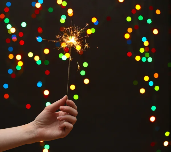 Beautiful sparkler in woman hand on garland background — Stock Photo, Image