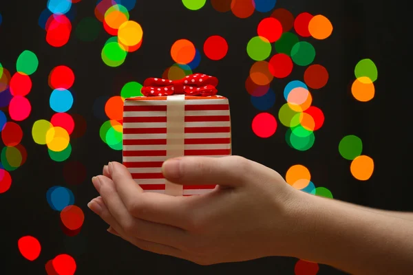 Mano de mujer con caja de regalo, sobre fondo de guirnalda — Foto de Stock