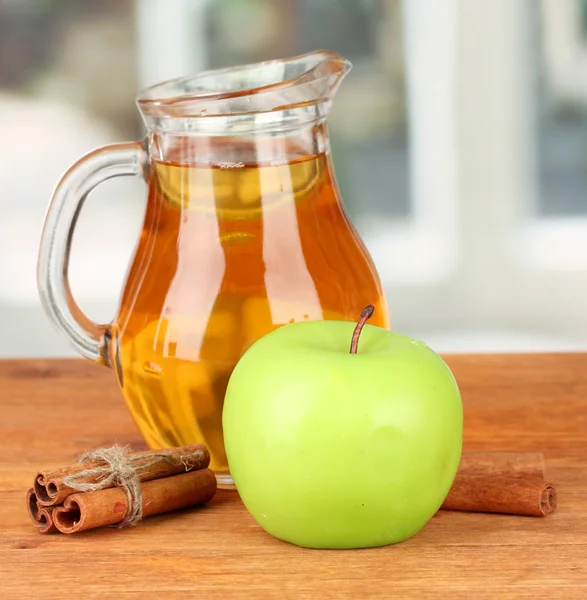 Полный кувшин яблочного сока и яблока на деревянном столе на ярком фоне — стоковое фото