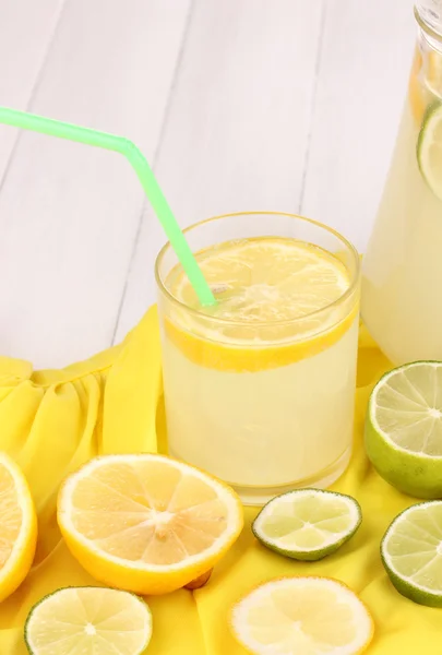 Citrus saft i glas och tillbringare med citrus runt på gult tyg på vita träbord närbild — Stockfoto