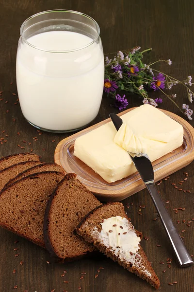 Масло на деревянном держателе в окружении хлеба и молока на деревянном столе крупным планом — стоковое фото