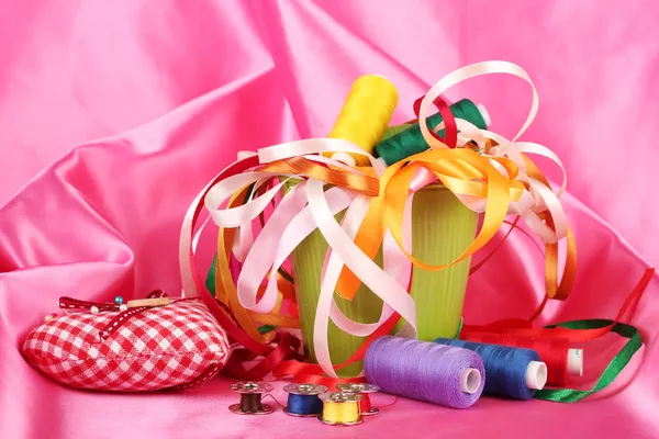 Color bucket with multicolor ribbons and thread on pink fabric background — Stock Photo, Image