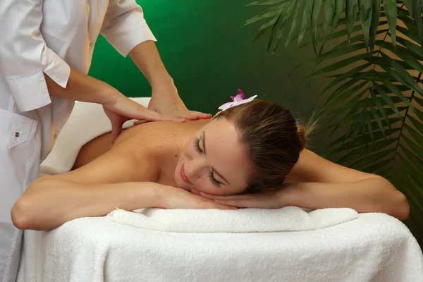 Beautiful young woman in spa salon getting massage, on green background — Stock Photo, Image