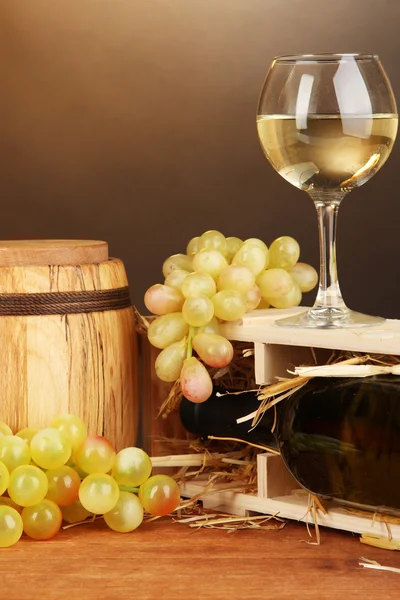 Caixa de madeira com garrafa de vinho, barril, vinho e uva em mesa de madeira sobre fundo marrom — Fotografia de Stock