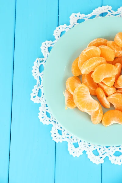 Tasty mandarine's slices on color plate on blue background — Stock Photo, Image