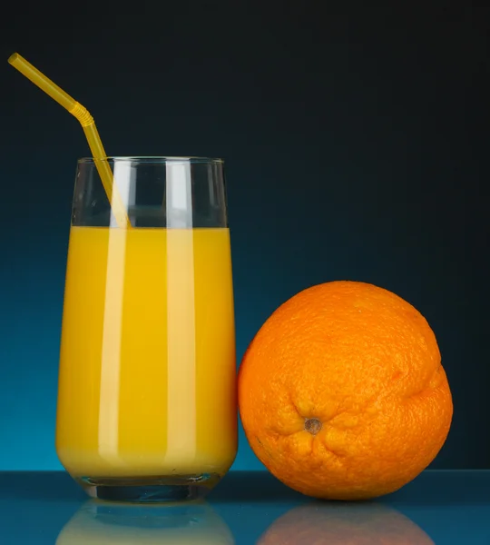 Heerlijke sinaasappelsap in glas en oranje ernaast op donker blauwe achtergrond — Stockfoto