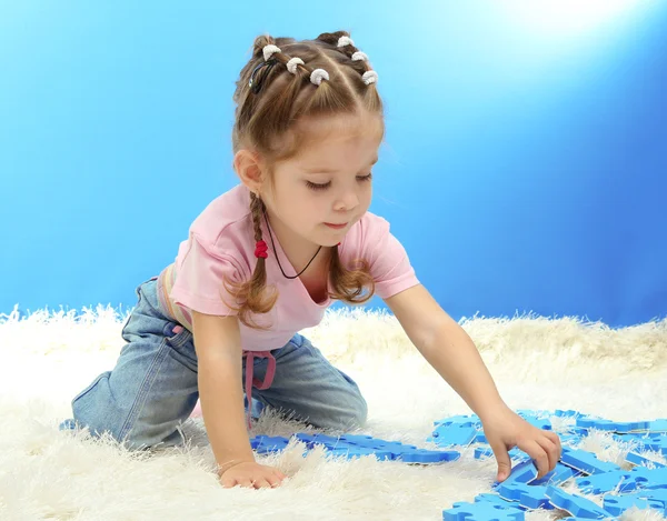 Niedliches kleines Mädchen, das mit Puzzles spielt, auf blauem Hintergrund — Stockfoto