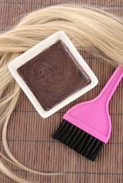 Tintura de cabelo na tigela e escova para coloração de cabelo no tapete de bambu marrom, close-up — Fotografia de Stock