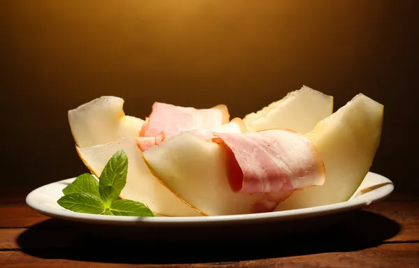 Parma ham and melon, on wooden table, on brown background — Stock Photo, Image