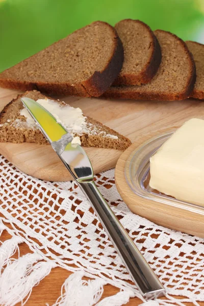 Butter on wooden holder surrounded by bread and milk on natural background close-up — Stock Photo, Image