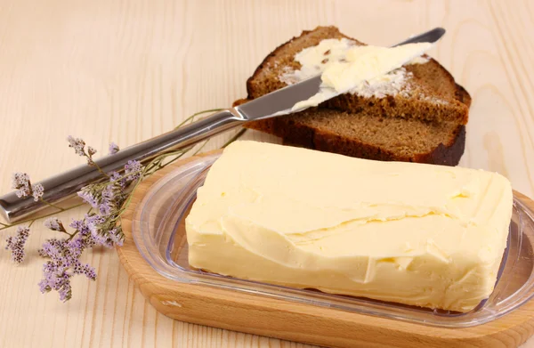 Масло на деревянном держателе и хлеб на деревянном столе крупным планом — стоковое фото