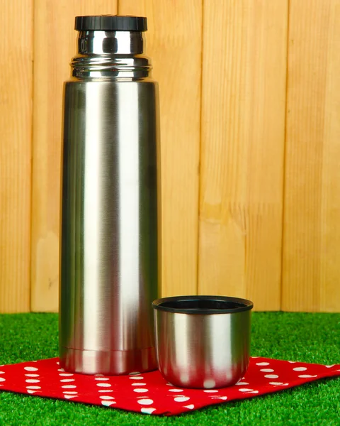 Metal thermos on grass on wooden background — Stock Photo, Image