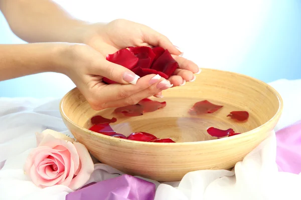 Woman hands with wooden bowl of water with petals, on blue background — Stock Photo, Image