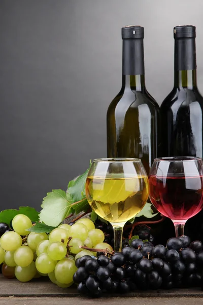 Flaschen und Gläser mit Wein und Trauben auf grauem Hintergrund — Stockfoto