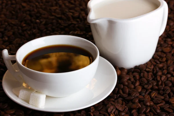 Eine Tasse starken Kaffee und süße Sahne auf Kaffeebohnen aus nächster Nähe — Stockfoto