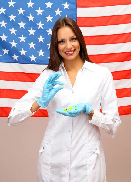 Retrato de médica ou cientista mostrando e analisando pílulas sobre fundo bandeira americana — Fotografia de Stock