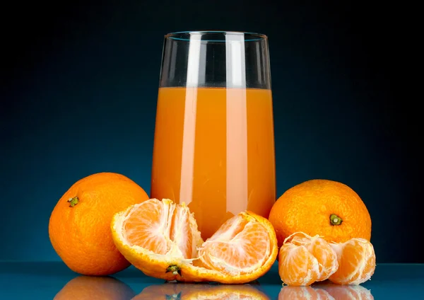 Delicioso suco de tangerina em vidro e mandarinas ao lado dele no fundo azul escuro — Fotografia de Stock