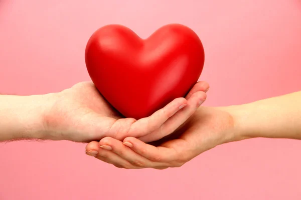 Coração vermelho em mãos de mulher e homem, em fundo rosa — Fotografia de Stock