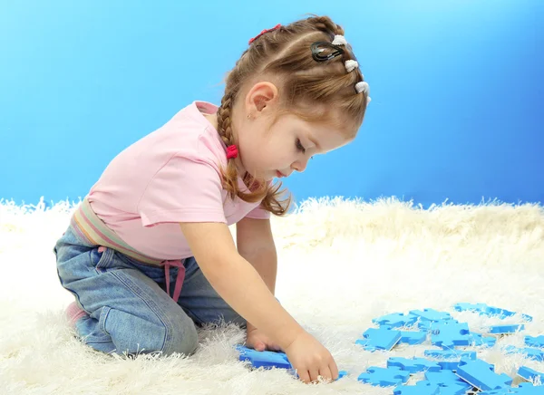 Schattig klein meisje spelen met puzzels, op blauwe achtergrond — Stockfoto