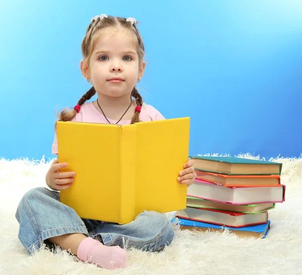 Mignonne petite fille avec des livres colorés, sur fond bleu — Photo