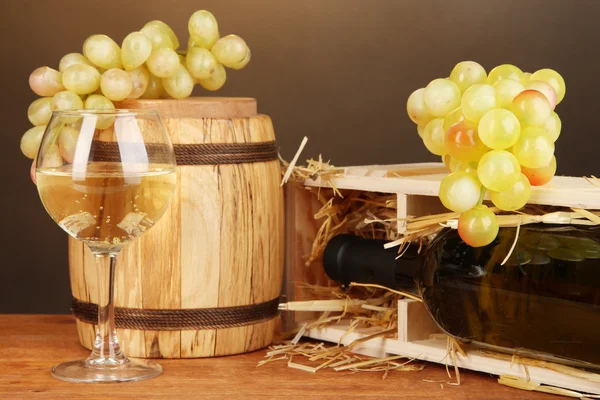 Wooden case with wine bottle, barrel, wineglass and grape on wooden table on brown background Stock Photo