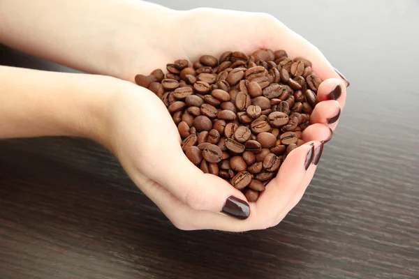 Manos femeninas con granos de café, sobre fondo de madera —  Fotos de Stock