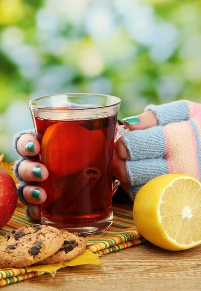 Mani che tengono tazza di bevanda calda e foglie autunnali, su sfondo verde — Foto Stock