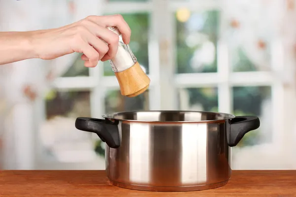 Hand adding salt using salt shaker on bright background — Stock Photo, Image