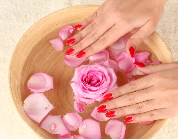 Vrouw handen met houten kom met water met bloemblaadjes — Stockfoto