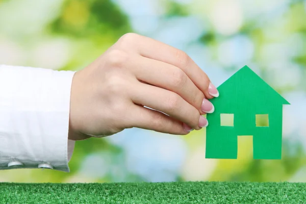 Concept: woman hand with paper house on green background, close up — Stock Photo, Image