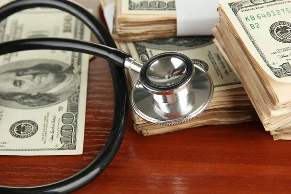 Healthcare cost concept: stethoscope and dollars on wooden background — Stock Photo, Image