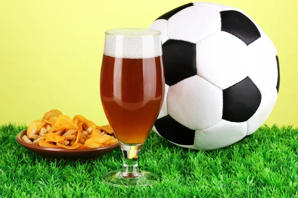 Copo de cerveja com bola de futebol na grama no fundo verde — Fotografia de Stock
