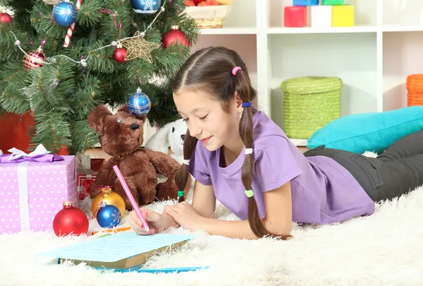 Menina escrevendo carta para o Papai Noel perto da árvore de Natal — Fotografia de Stock