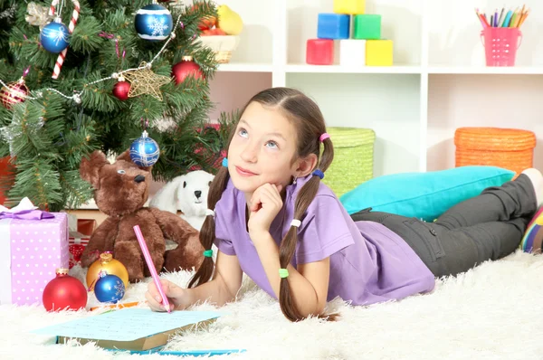 Klein meisje schrijven brief aan de Kerstman in de buurt van de kerstboom — Stockfoto