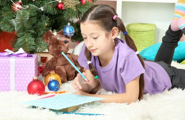 Liten flicka skriva brev till santa nära julgran — Stockfoto