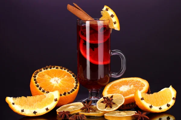 Fragrant mulled wine in glass with spices and oranges around on purple background — Stock Photo, Image