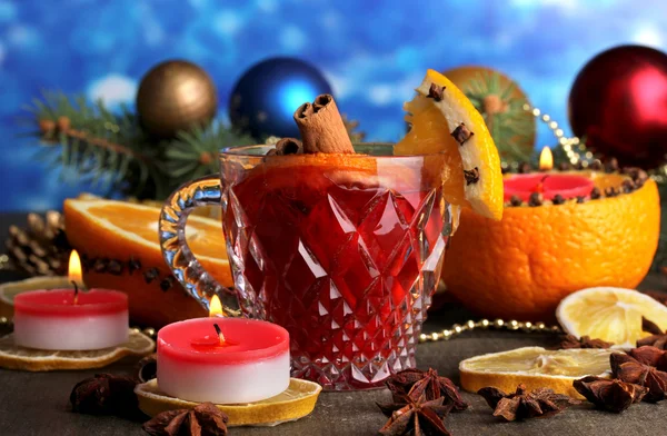 Geurige glühwein in glas met specerijen en sinaasappelen rond op houten tafel op blauwe achtergrond — Stockfoto