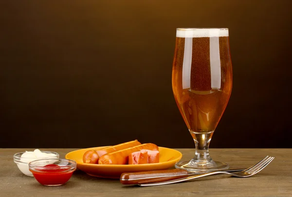 Bier en gegrilde worstjes op houten tafel op bruine achtergrond — Stockfoto