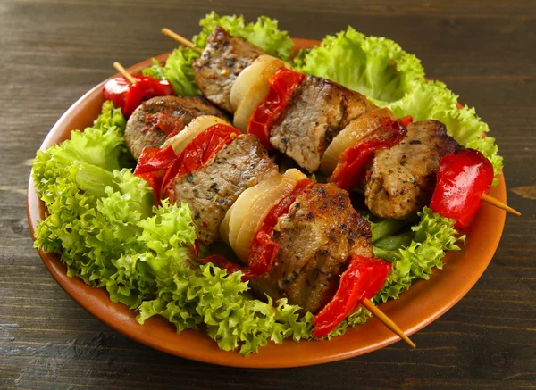 Lekker gegrild vlees en groenten op spies op bord, op houten tafel — Stockfoto