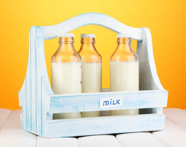 Milch in Flaschen in Holzkiste auf Holztisch auf orangefarbenem Hintergrund — Stockfoto