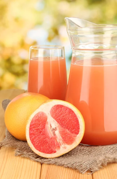 Volles Glas und Krug mit Grapefruitsaft und Grapefruits auf Holztisch im Freien — Stockfoto