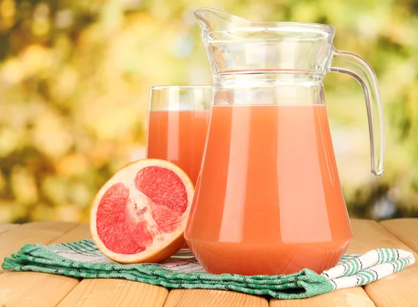Full glass and jug of grapefruit juice and grapefruits on wooden table outdoor — Stock Photo, Image