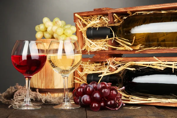 Caja de madera con botellas de vino, barril, copas de vino y uva sobre mesa de madera sobre fondo gris —  Fotos de Stock