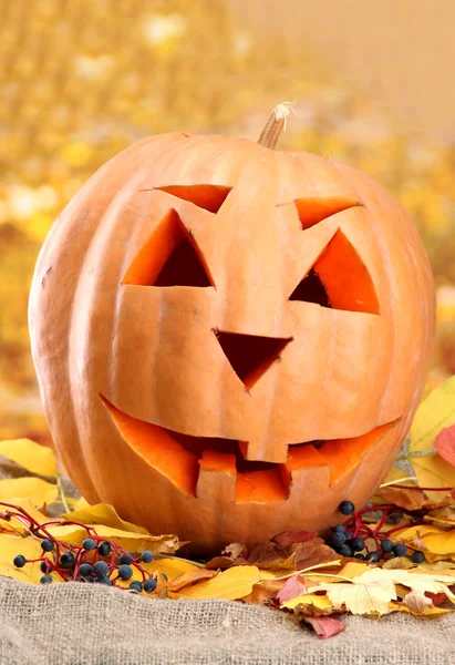 Halloween pumpkin and autumn leaves, on yellow background — Stock Photo, Image