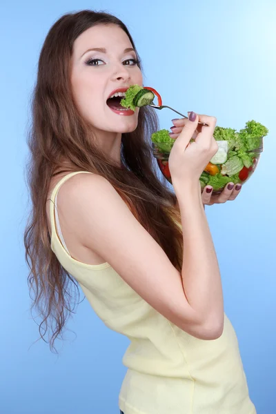 Mooie vrouw met plantaardige salade op blauwe achtergrond — Stockfoto