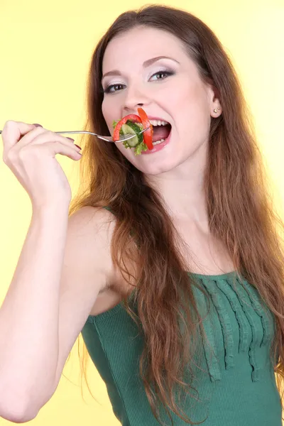 Mulher bonita comendo salada de legumes no fundo amarelo — Fotografia de Stock