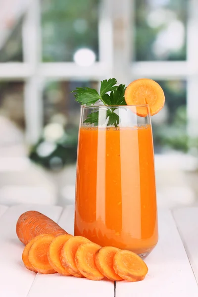Стекло морковного сока на деревянном столе, на фоне окна — стоковое фото